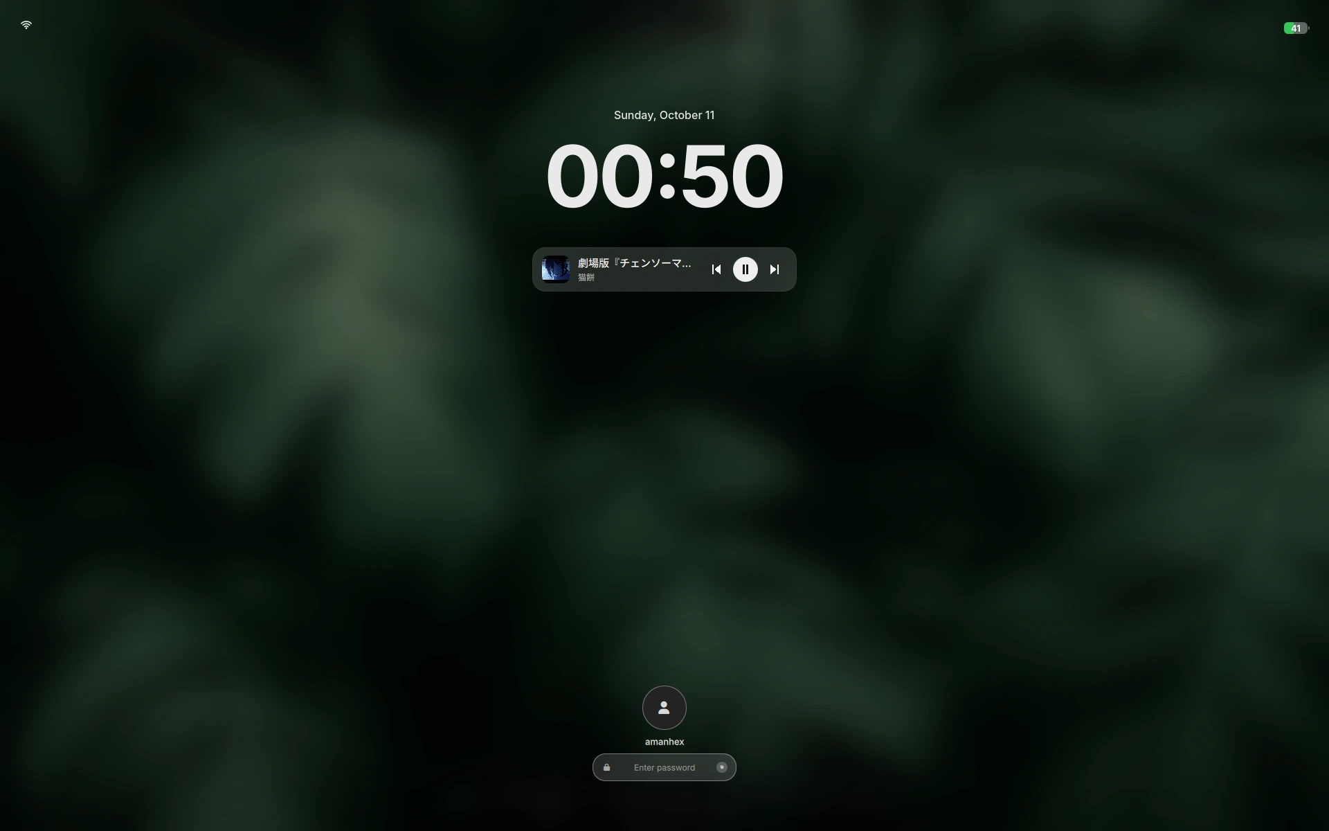 The Ukishima lock screen: the date and a large clock over a blurred still of the desktop, a media card with album art and transport controls beneath the clock, the avatar and password field centred below, and battery and Wi-Fi readouts in the corners.